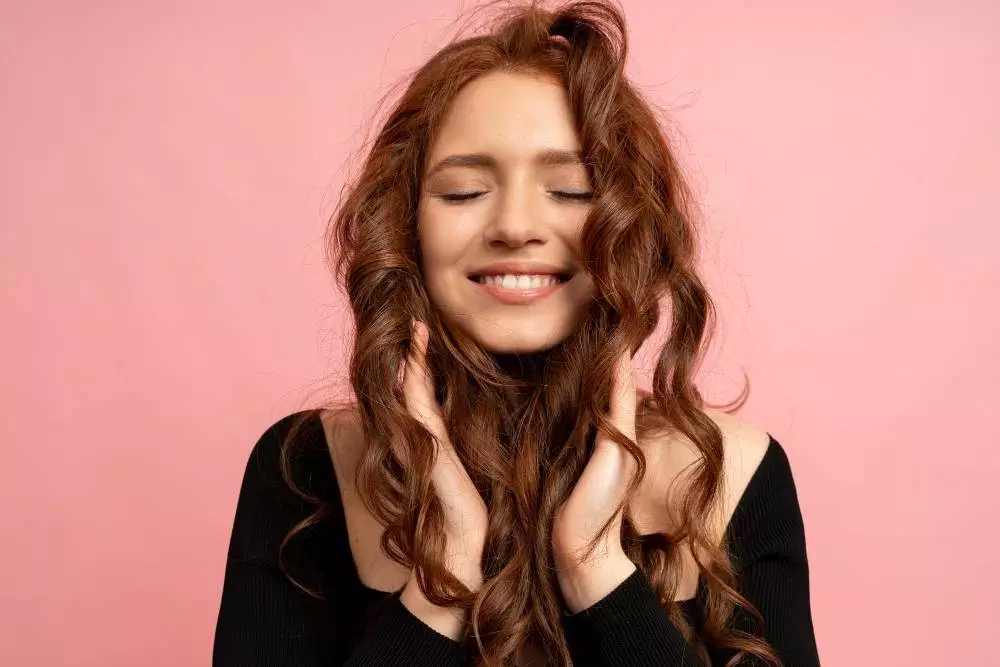 beautiful red head woman with close eyes posing pink wall wavy hairs perfect smile